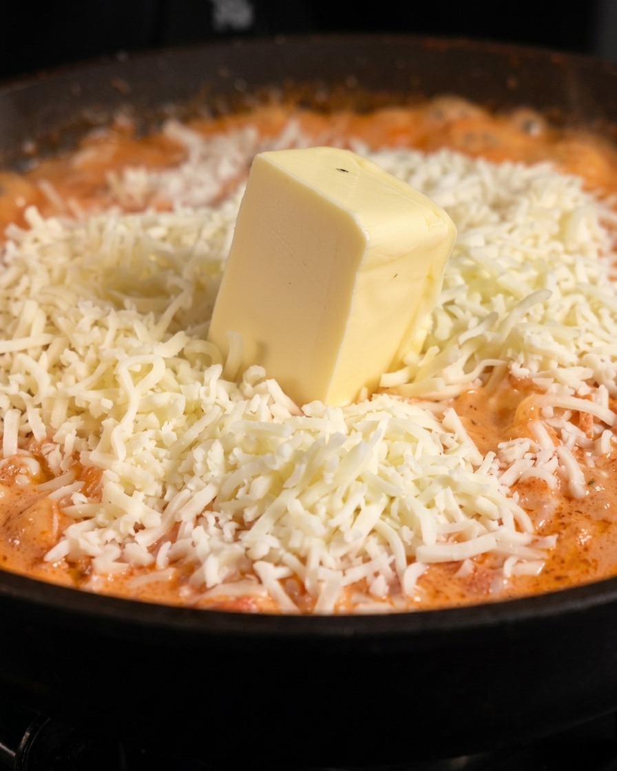 Un cubetto di burro morbido adagiato su una pioggia di mozzarella bianca grattugiata sopra la pasta allarancia.