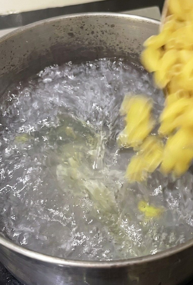 Maccheroni versati da una ciotola in una pentola dacciaio con acqua appliata e bollente sul fuoco.