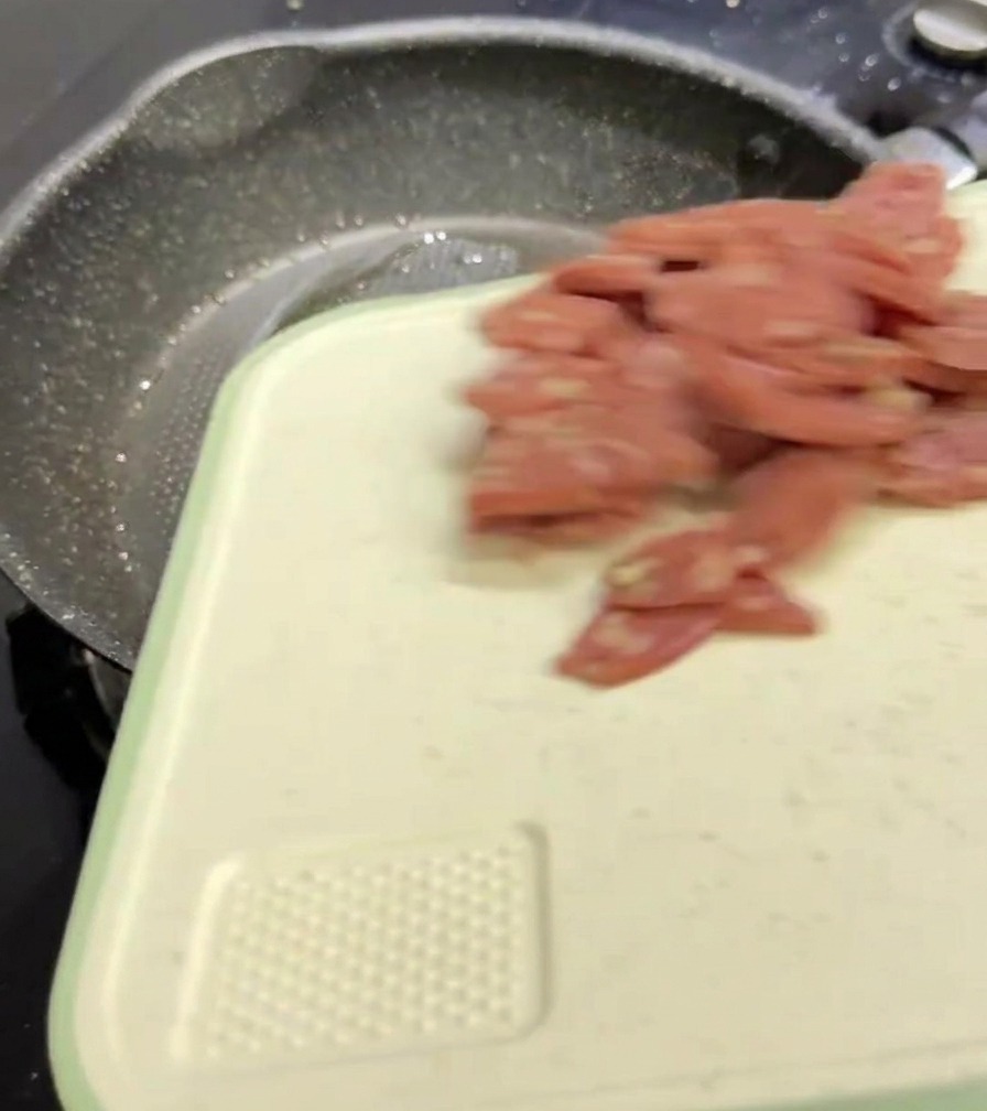 Cubetti di salame che cadono da un tagliere bianco in una padella antiaderente scura.