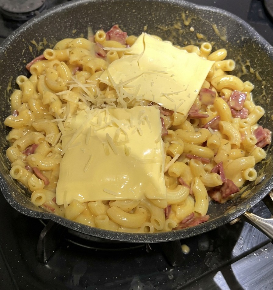 Due fette di formaggio fuso e formaggio grattugiato adagiati sopra la pasta in padella.