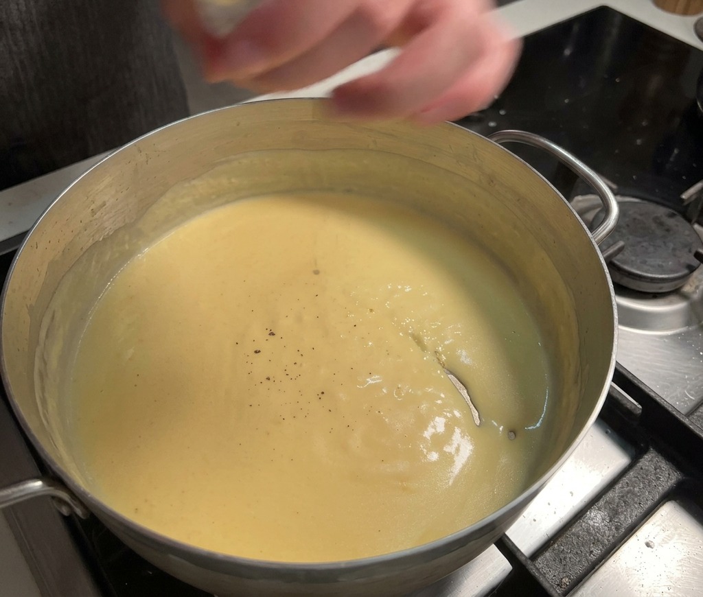 Pepe nero fresco macinato in una salsa al formaggio gialla densa e cremosa che sobbolle in padella.