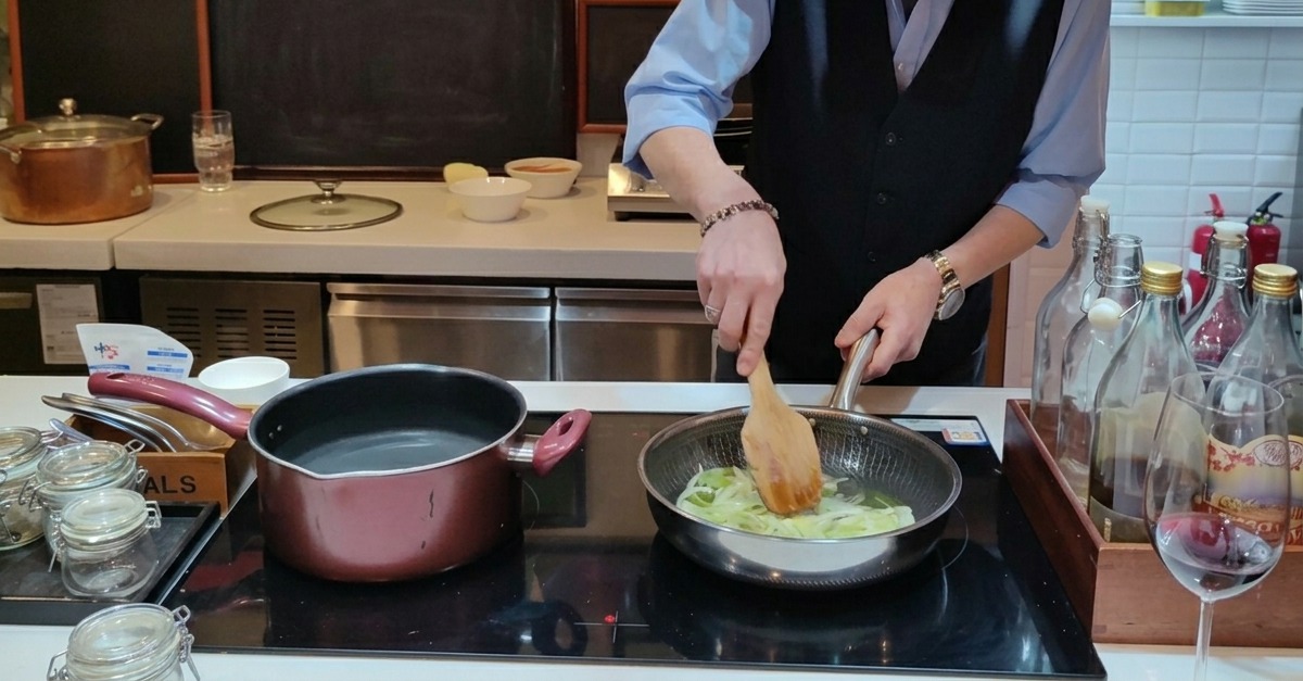 Cipolle tagliate sottili che soffriggono in una padella con olio doliva, mescolate con una spatola di legno.