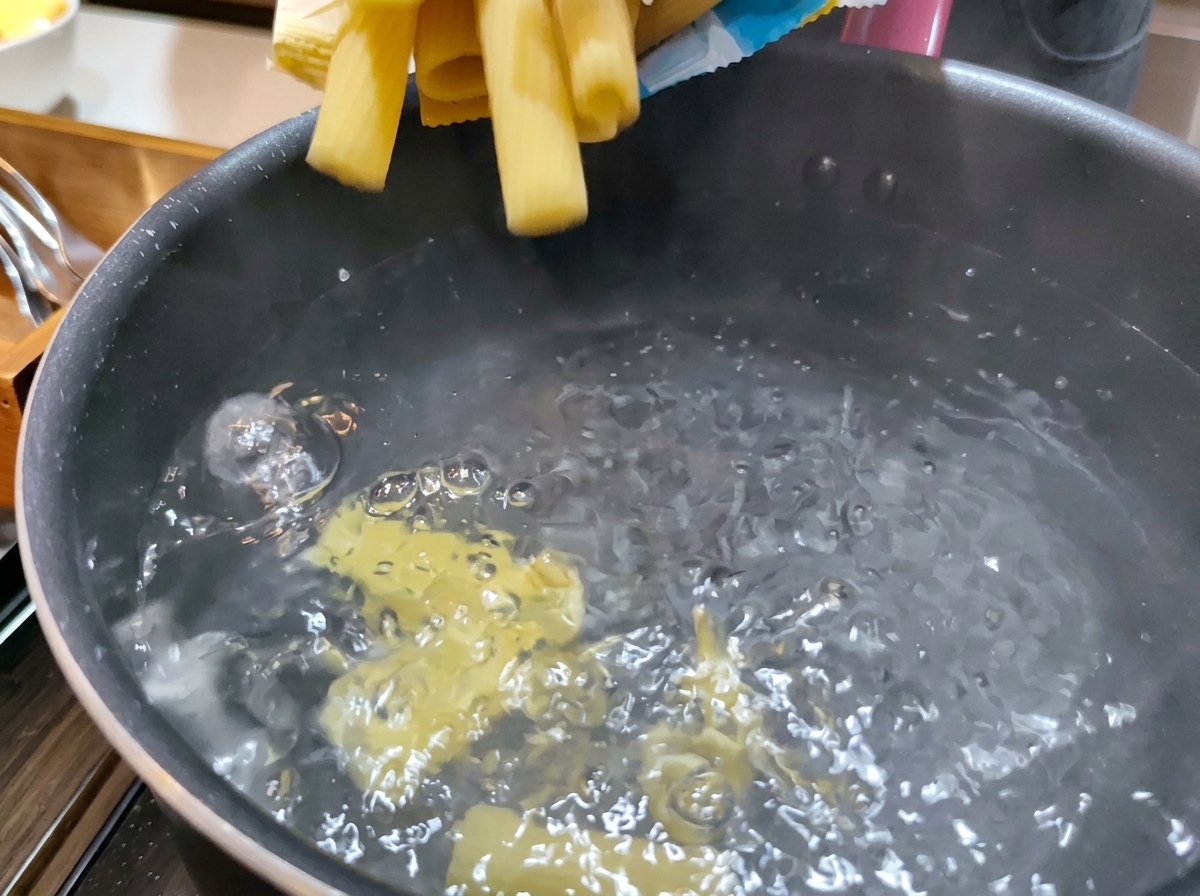 Rigatoni secchi e gialli tuffati in una pentola di acqua bollente e spumeggiante.