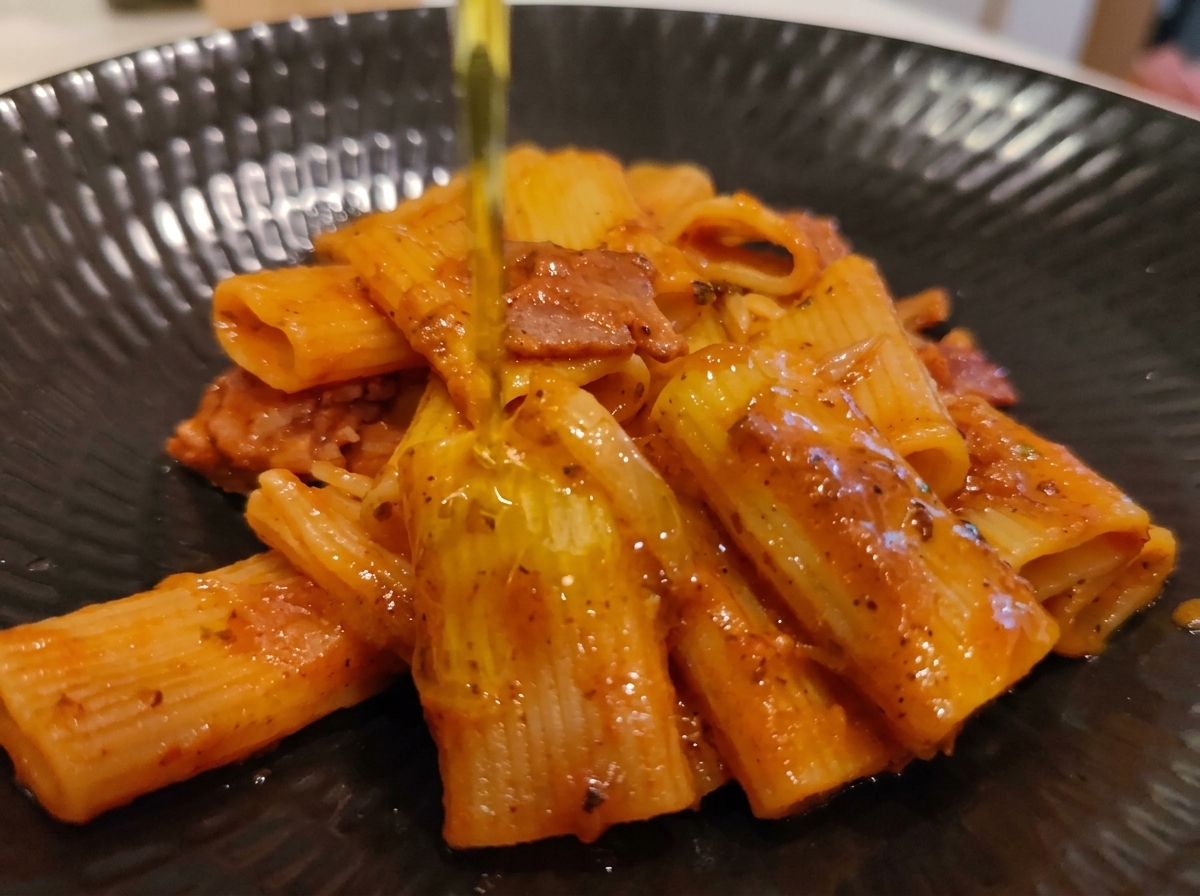 Un filo dolio extravergine doliva versato su una porzione impiattata di rigatoni allAmatriciana.