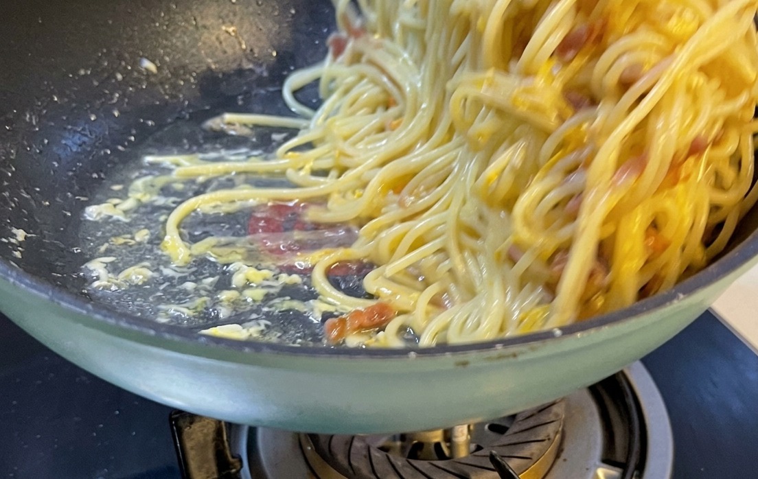 Una porzione splendidamente impiattata di spaghetti alla carbonara su un piatto di ceramica bianca, guarnita con formaggio grattugiato e pepe.