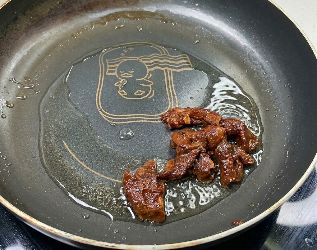Straccetti di maiale marinati che cuociono in padella con olio, mostrando un colore brunito e una superficie lucida.
