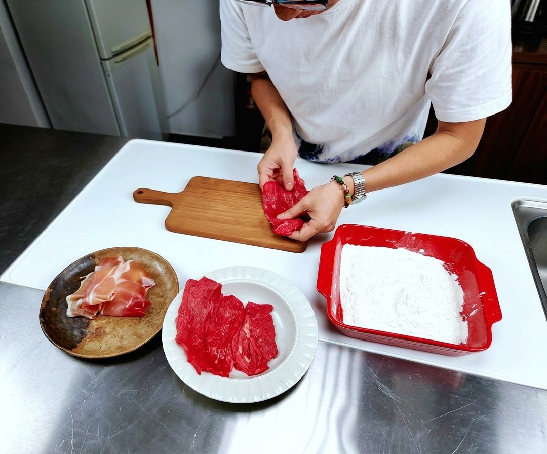 Sottili fettine di vitello crudo disposte su un tagliere di legno chiaro.