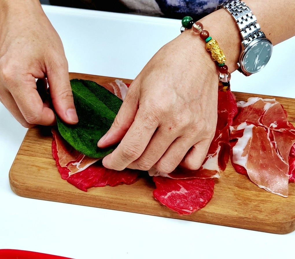 Mani che posizionano una foglia di salvia fresca al centro della carne con il prosciutto.
