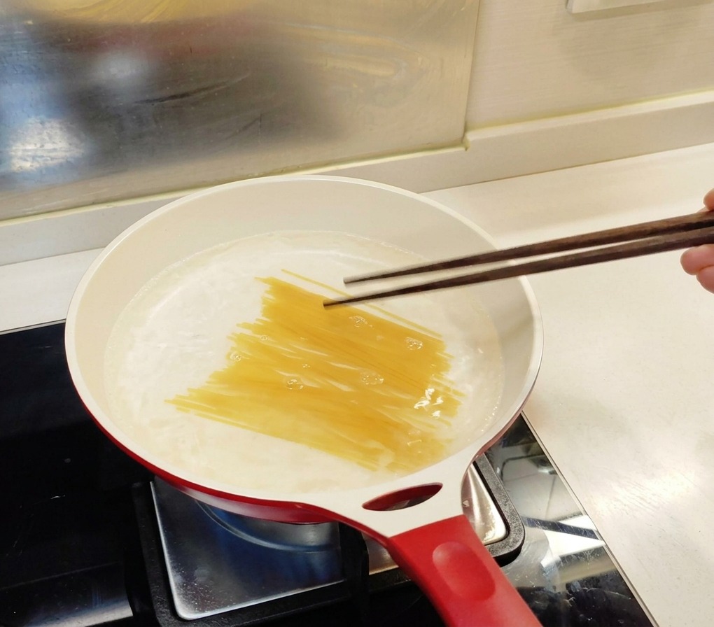 Spaghetti crudi immersi in una pentola dacqua bollente e girati delicatamente con le bacchette.