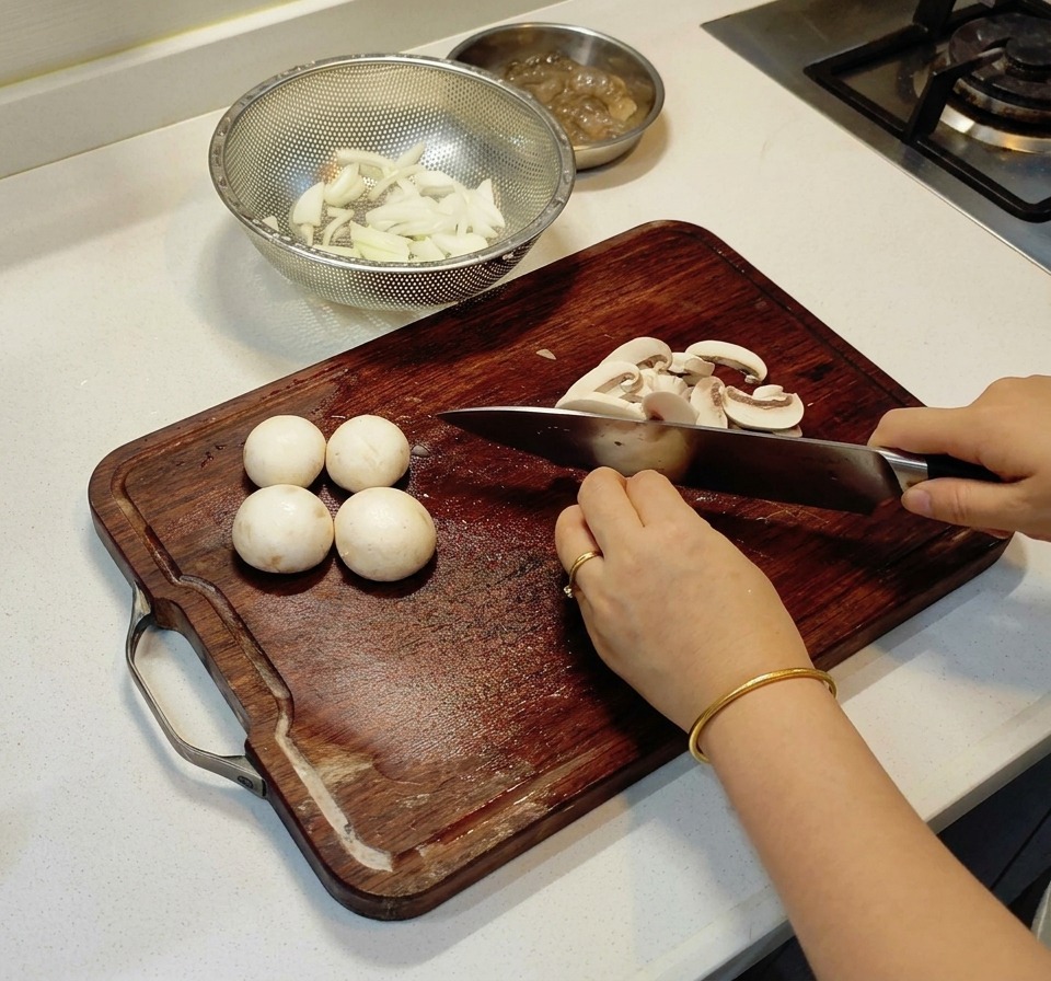 Una persona che affetta funghi champignon bianchi a strisce sottili su un tagliere di legno.