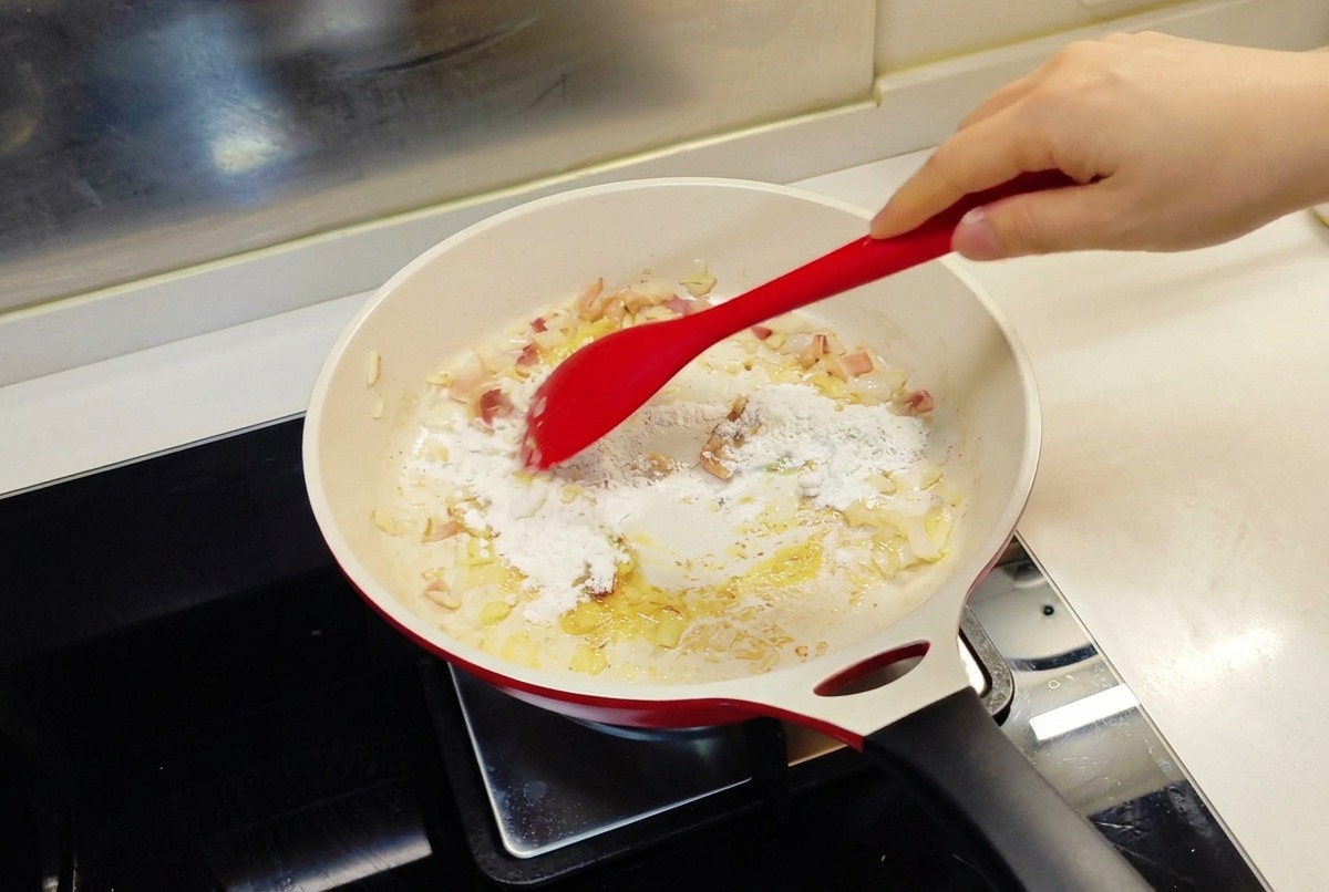 Una spatola rossa che incorpora la farina nella padella con la cipolla saltata e il burro fuso.