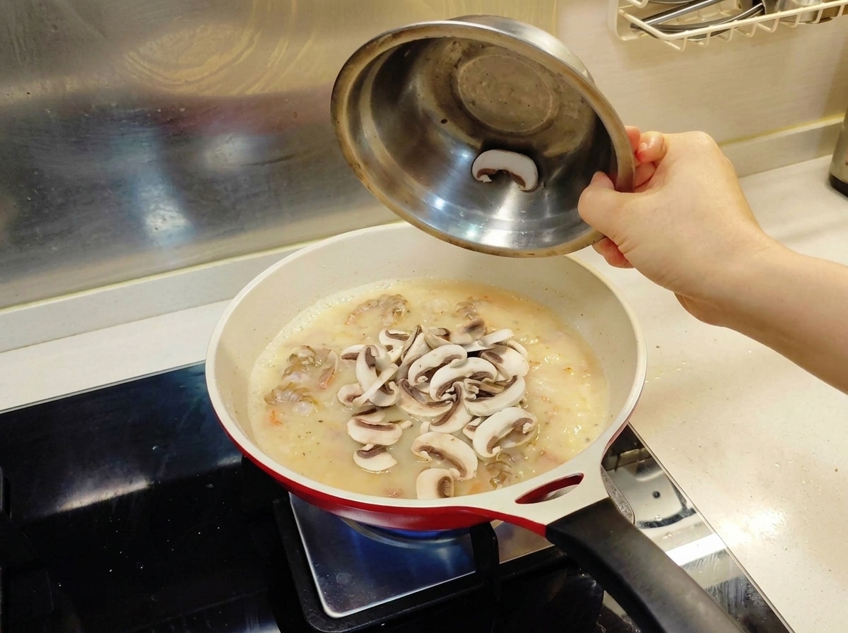 Fettine di funghi freschi versate da una ciotola di metallo in una padella contenente la base di salsa e i gamberi.