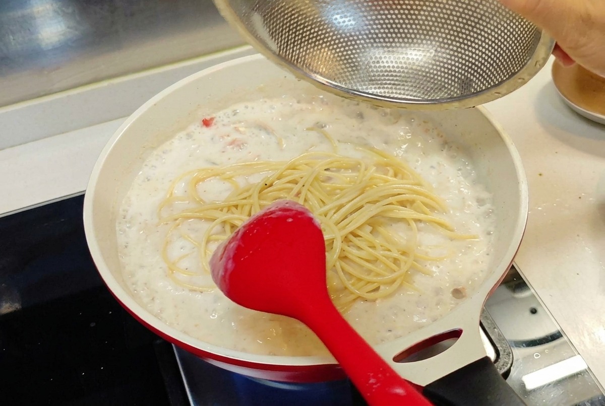 Spaghetti cotti trasferiti da uno scolapasta a rete direttamente nella padella con la salsa bianca cremosa.