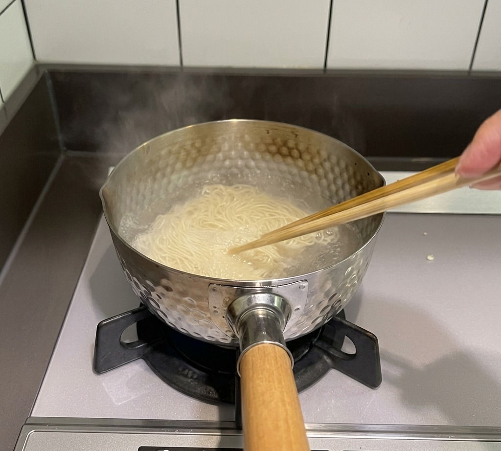 Delle bacchette di legno che mescolano i noodles sottili in una pentola dacqua bollente sul fuoco.