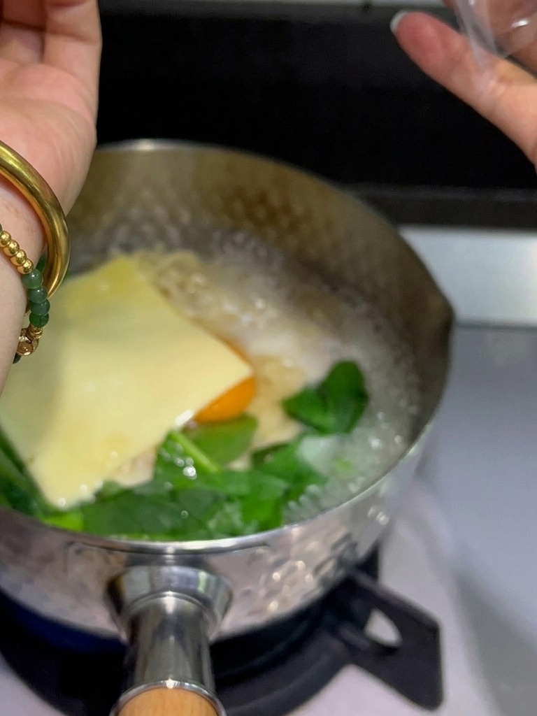 Fette di formaggio fuso giallo posizionate sopra luovo e i noodles nella pentola fumante.