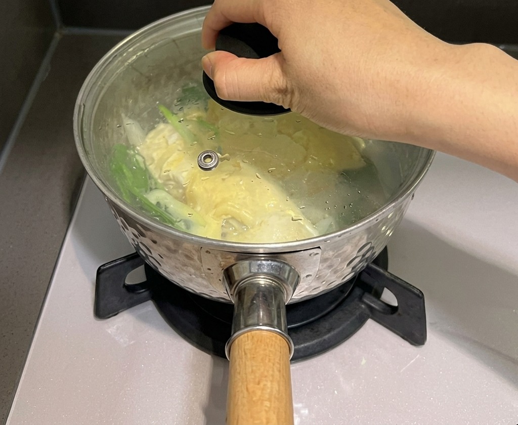 Una mano che posiziona un coperchio di vetro su una pentola di noodles e formaggio per trattenere il vapore.