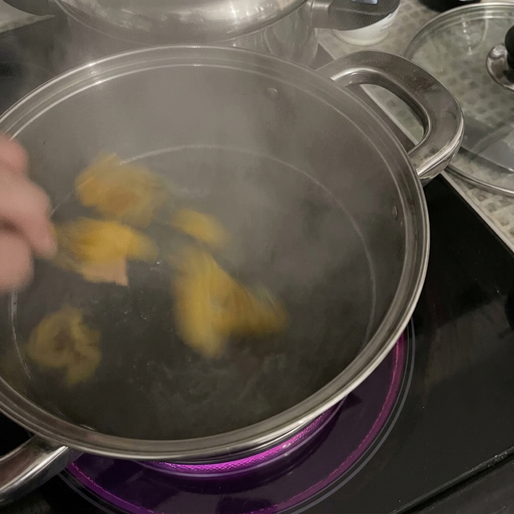 Una mano che versa i rigatoni in una pentola in acciaio inox con acqua bollente su un piano a induzione.