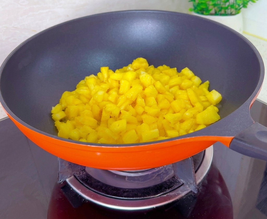 Cubetti di ananas giallo in cottura e riduzione dentro una padella arancione posizionata su un piano a induzione.