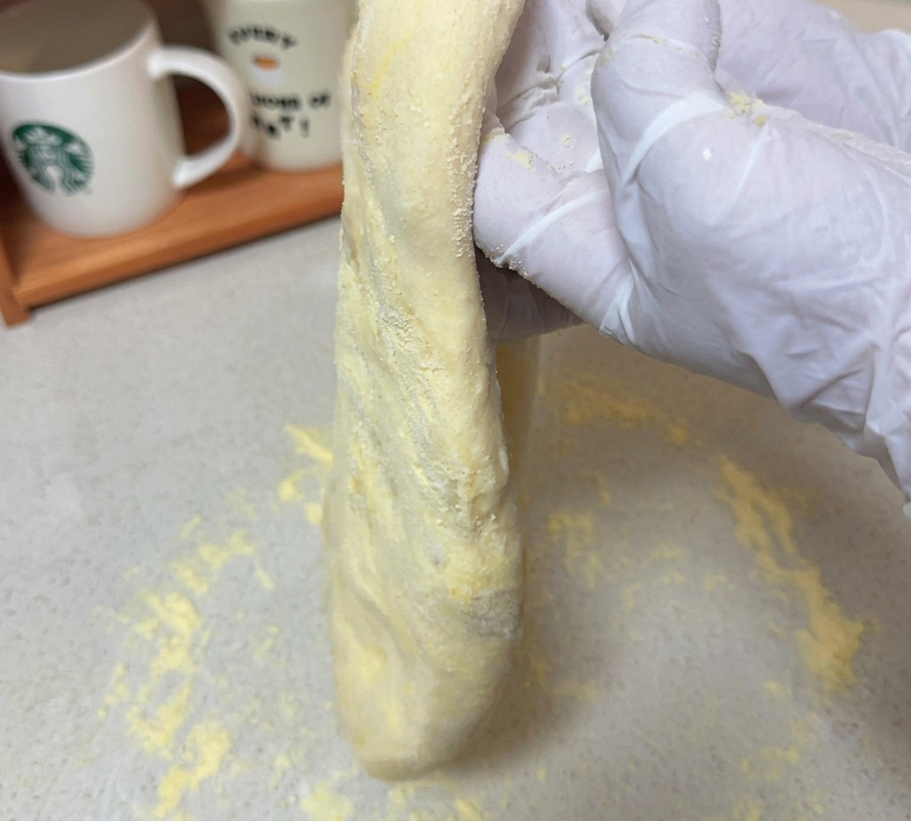 Un disco teso di impasto per pizza grezzo tenuto sollevato da mani con guanti sopra un piano di lavoro infarinato.