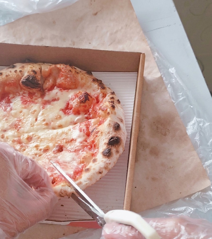 Una persona che usa delle forbici da cucina per tagliare la pizza calda allinterno di un cartone da asporto.