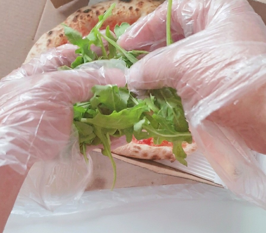 Mani che adagiano un ciuffo di rucola fresca al centro della pizza cotta nel cartone.