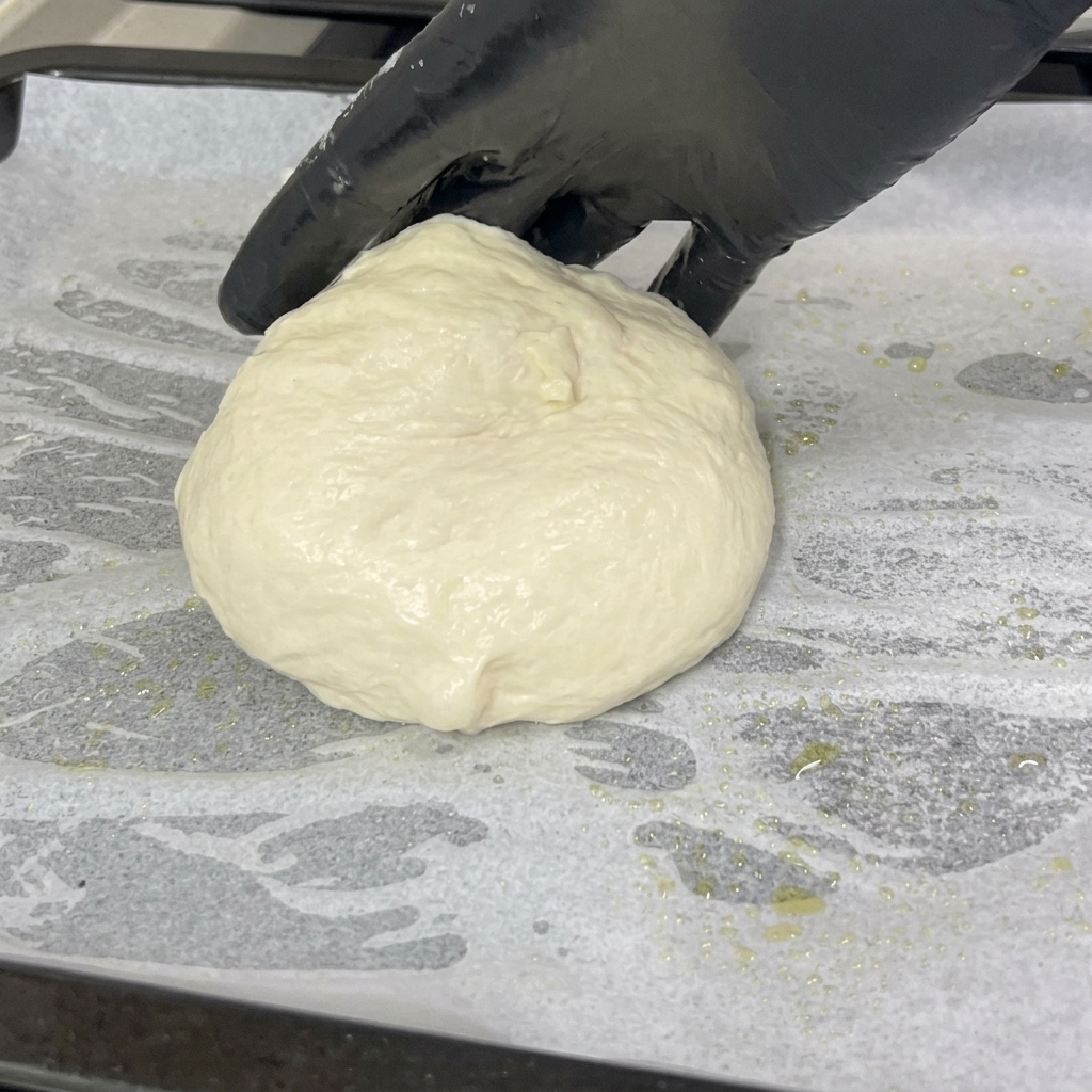 Una mano guantata adagia un panetto di impasto morbido su una teglia foderata di carta forno.