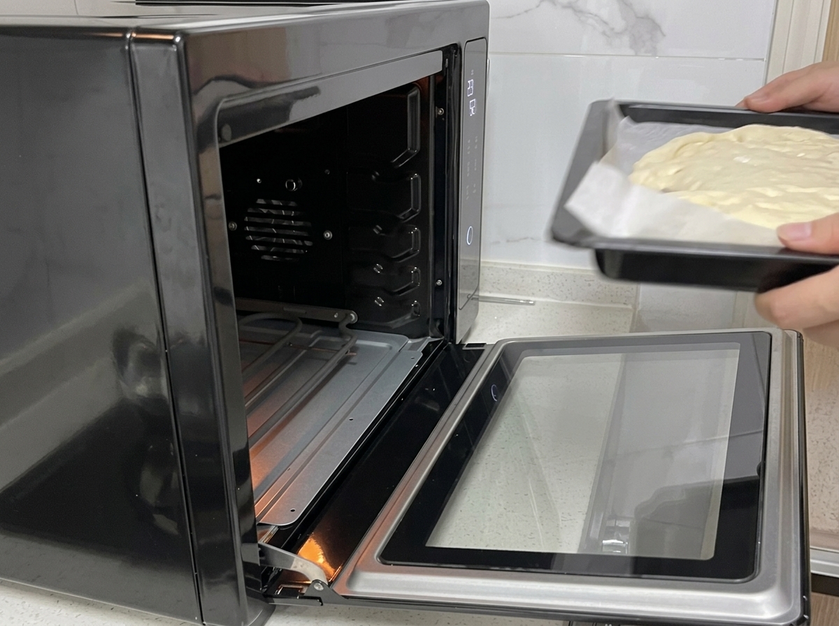 Mani che fanno scivolare una teglia con limpasto della pizza in un forno nero aperto.