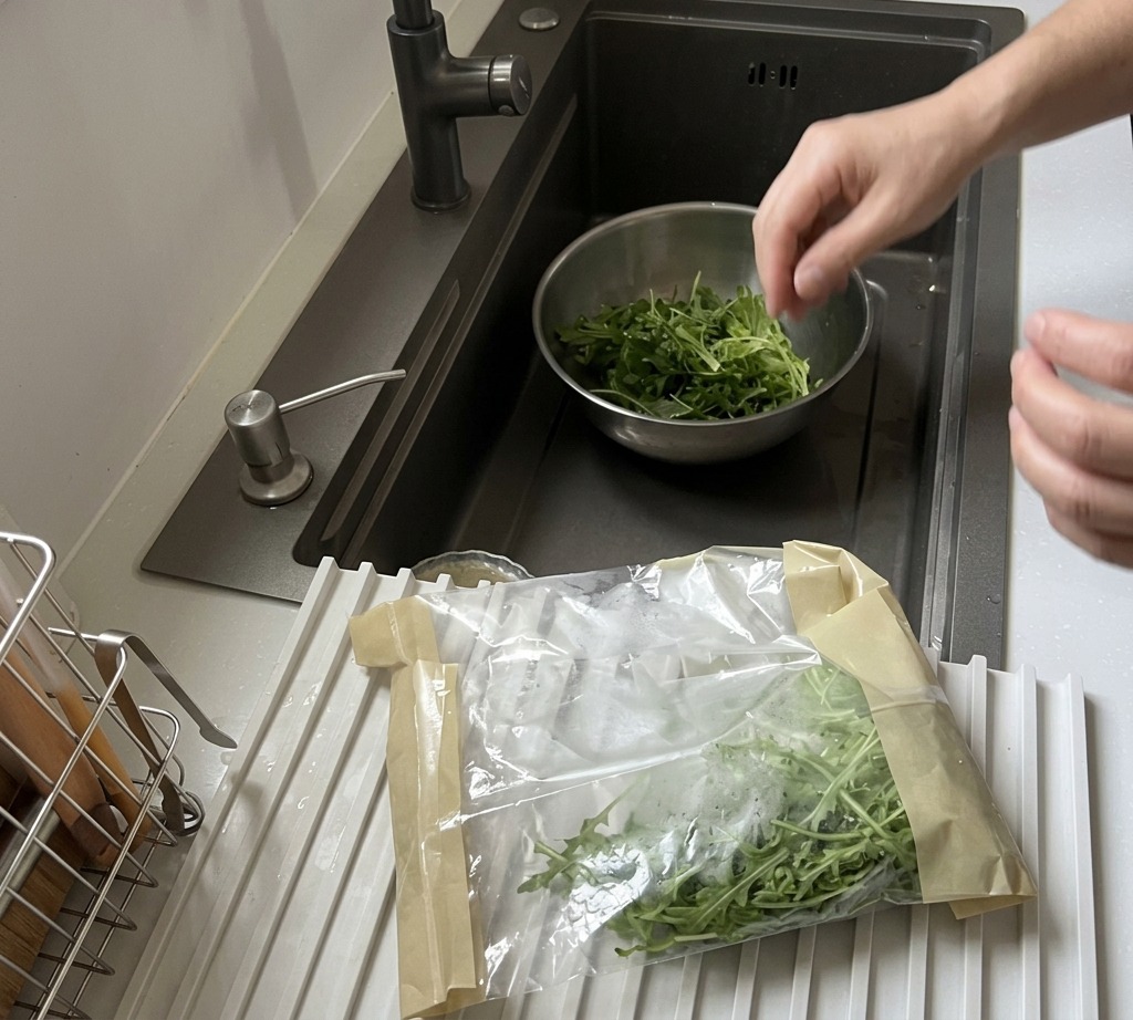 Foglie di rucola fresca lavate sotto lacqua corrente in una ciotola di acciaio.
