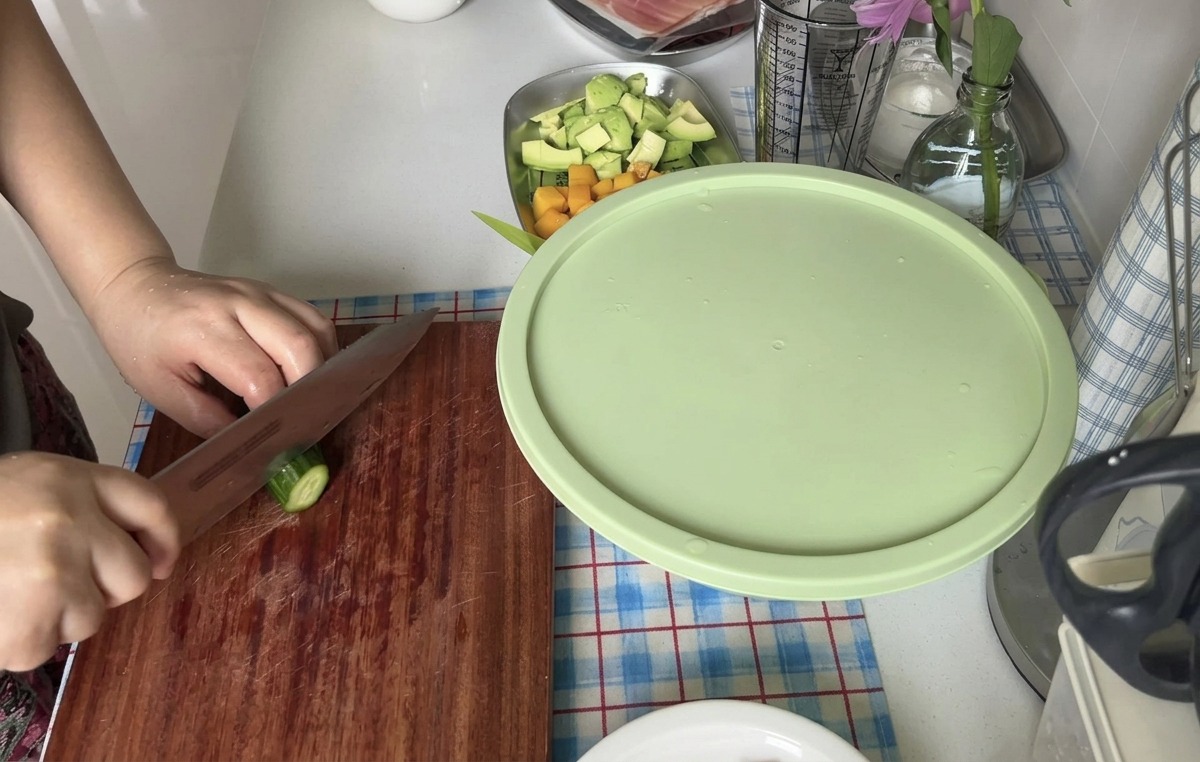 Una persona che taglia un cetriolo fresco a fette sottili con un coltello affilato su un tagliere di legno.