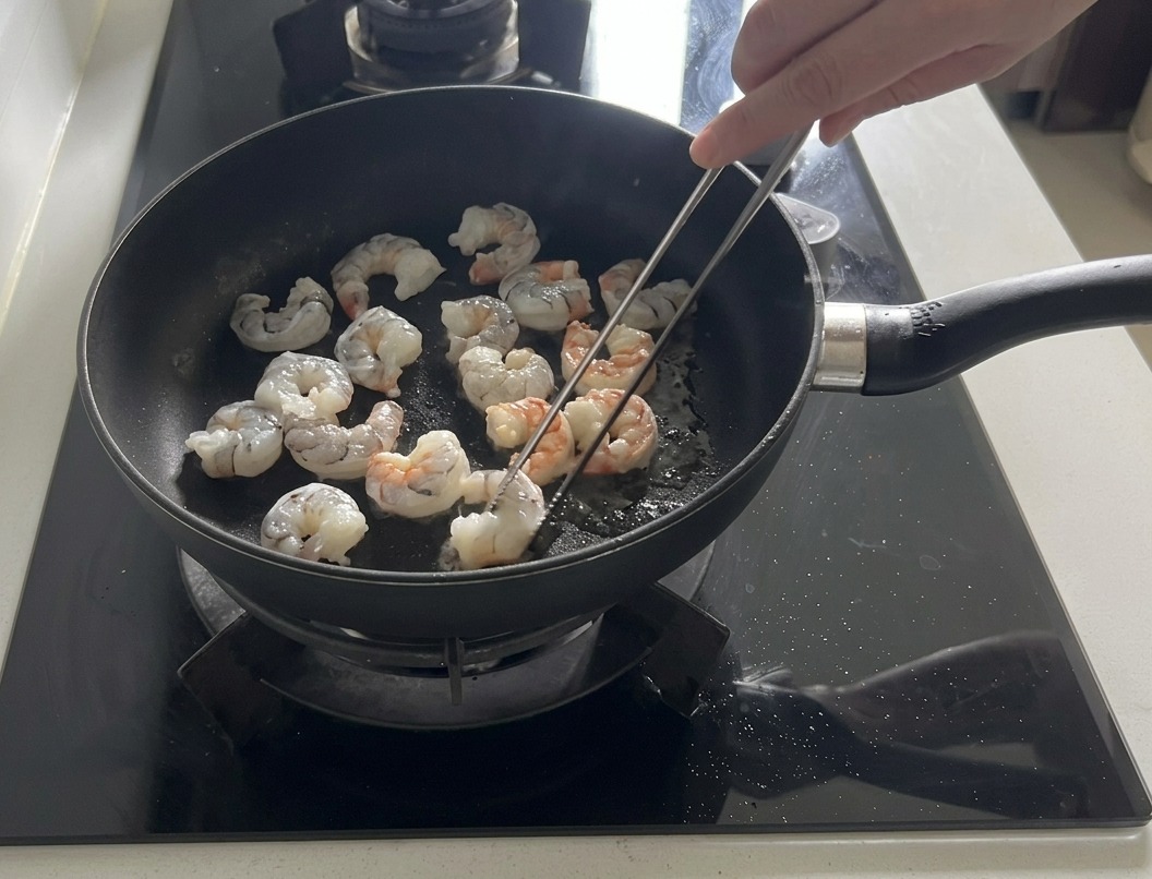 Gamberi freschi che saltano in una padella nera con olio doliva, alcuni dei quali diventano rosa e opachi.