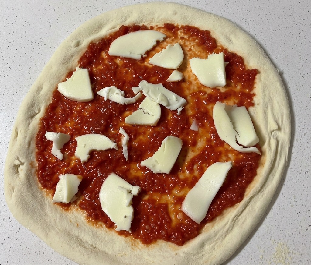Pezzi di mozzarella fresca spezzati a mano distribuiti sulla base della pizza coperta di pomodoro.