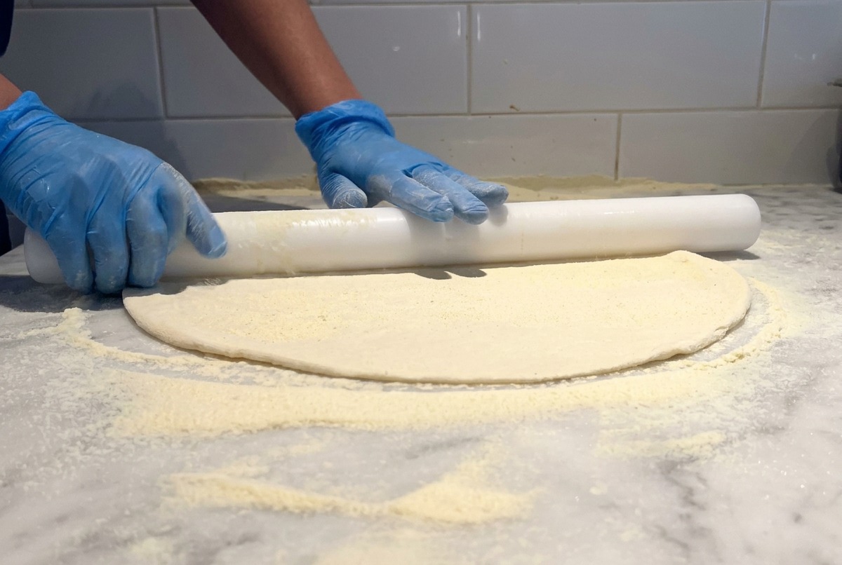 Un mattarello bianco utilizzato per stendere una base sottile di impasto per pizza su un tavolo di marmo infarinato.