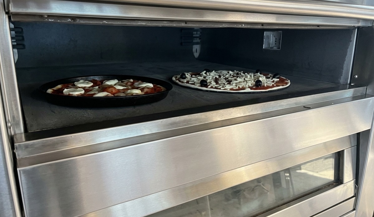 Due pizze in cottura sulla pietra refrattaria allinterno di un forno elettrico professionale in acciaio inox.