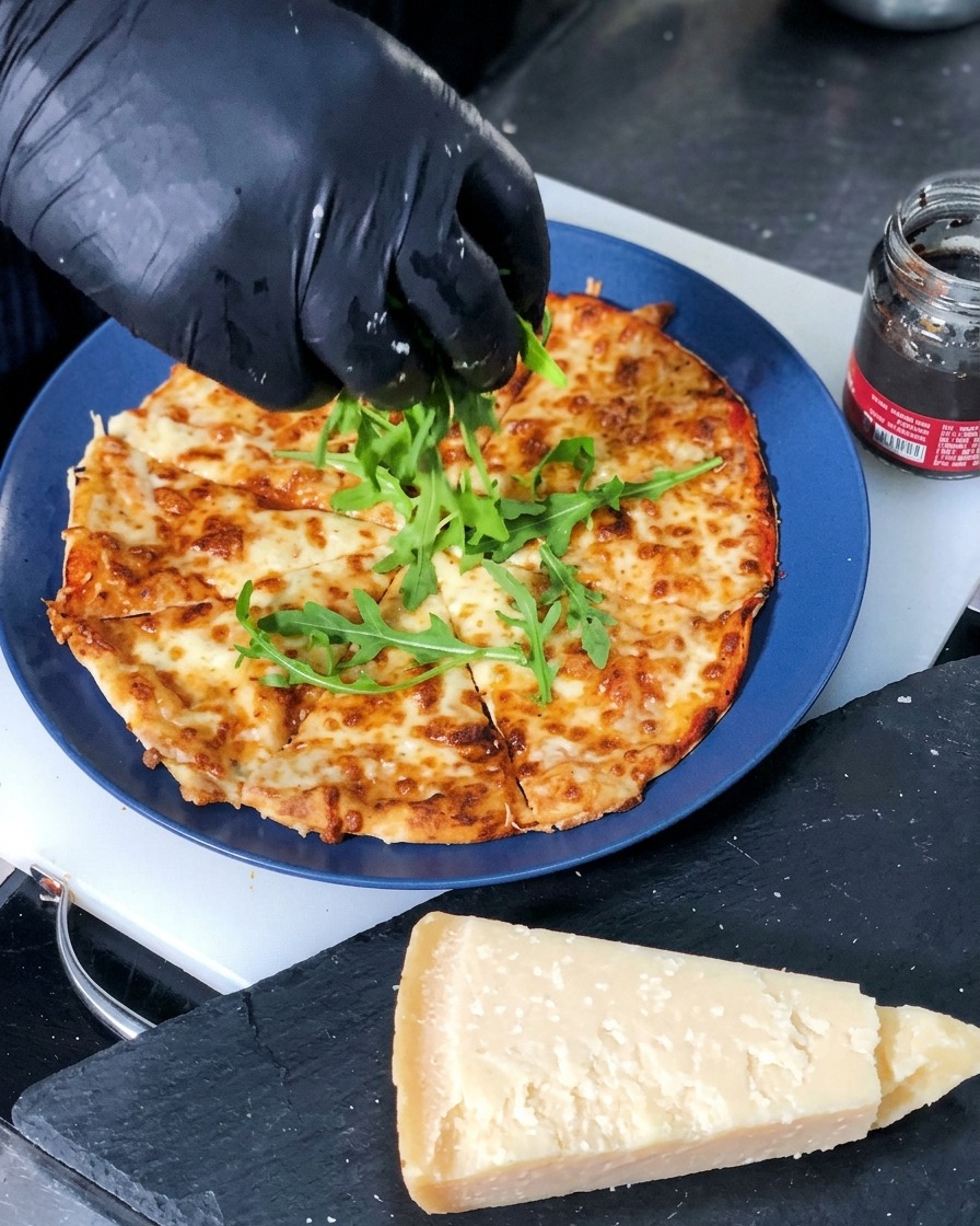 Foglie di rucola fresca verde che vengono adagiate al centro di una pizza al formaggio appena sfornata e tagliata a fette.