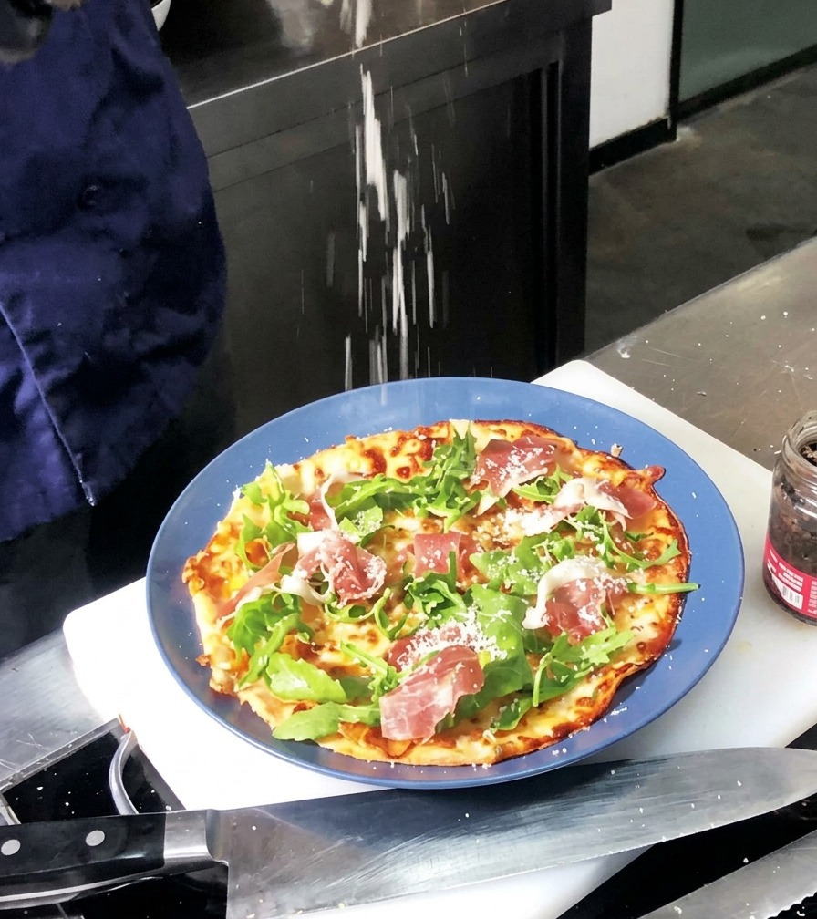 Parmigiano grattugiato finemente che viene spolverato sopra una pizza appena sfornata con rucola e prosciutto.