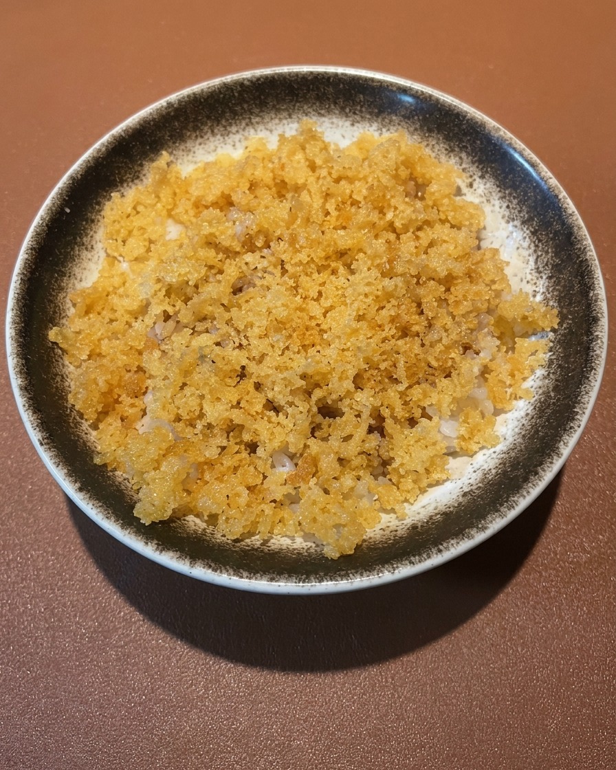Ciotola di riso guarnita con tempura di gamberi e verdure dorate.