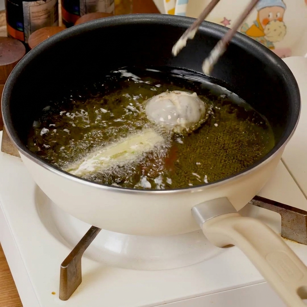 Pezzi di tempura impastellati che sfrigolano in una padella con olio caldo, dorandosi.