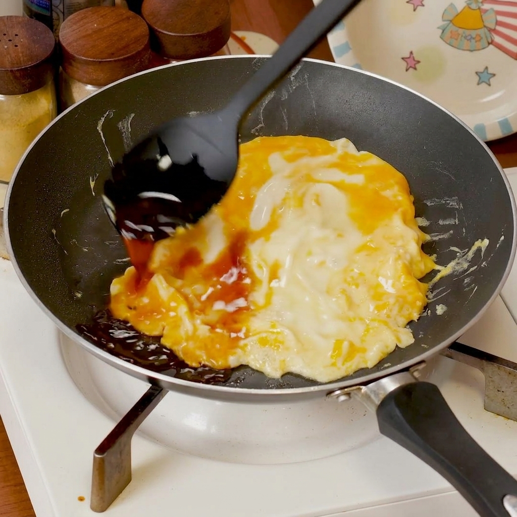 Salsa saporita versata sopra le uova strapazzate morbide che cuociono in padella.