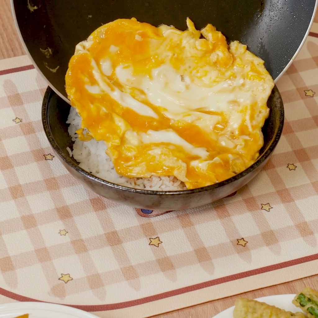 Uova strapazzate con salsa fatte scivolare sopra una ciotola di riso bianco.