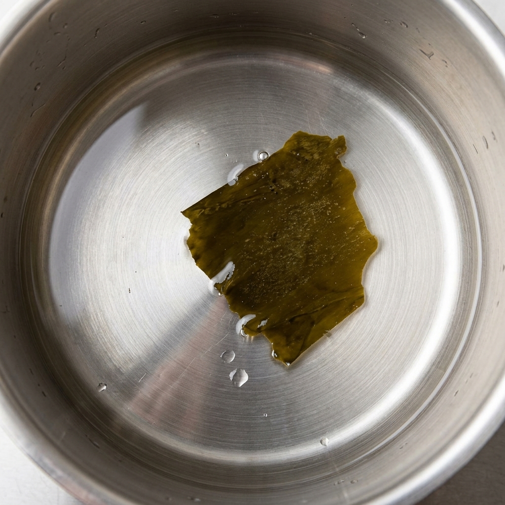 Un pezzo di alga kombu in infusione in una pentola con acqua fredda.
