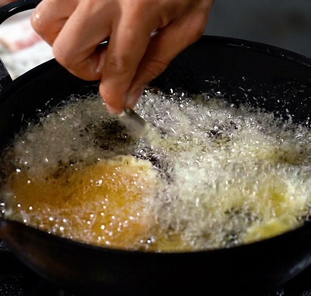 Gamberi che friggono in una pentola profonda con olio caldo, creando una crosta dorata.