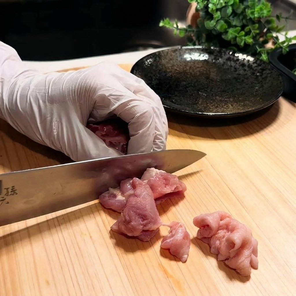 Primo piano di una coscia di pollo tagliata a piccoli pezzi su un tagliere di legno.