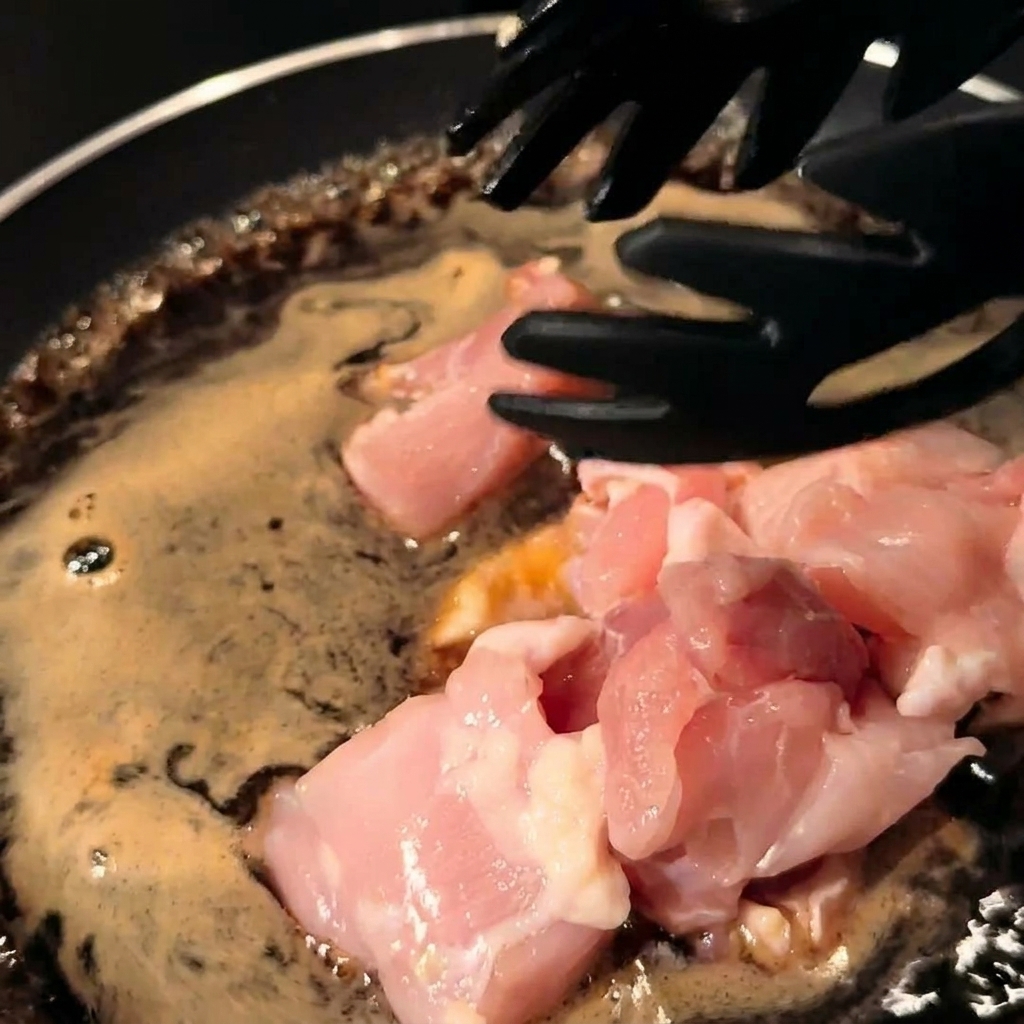 Pezzi di pollo e cipolle affettate mescolati nel sugo in una padella.