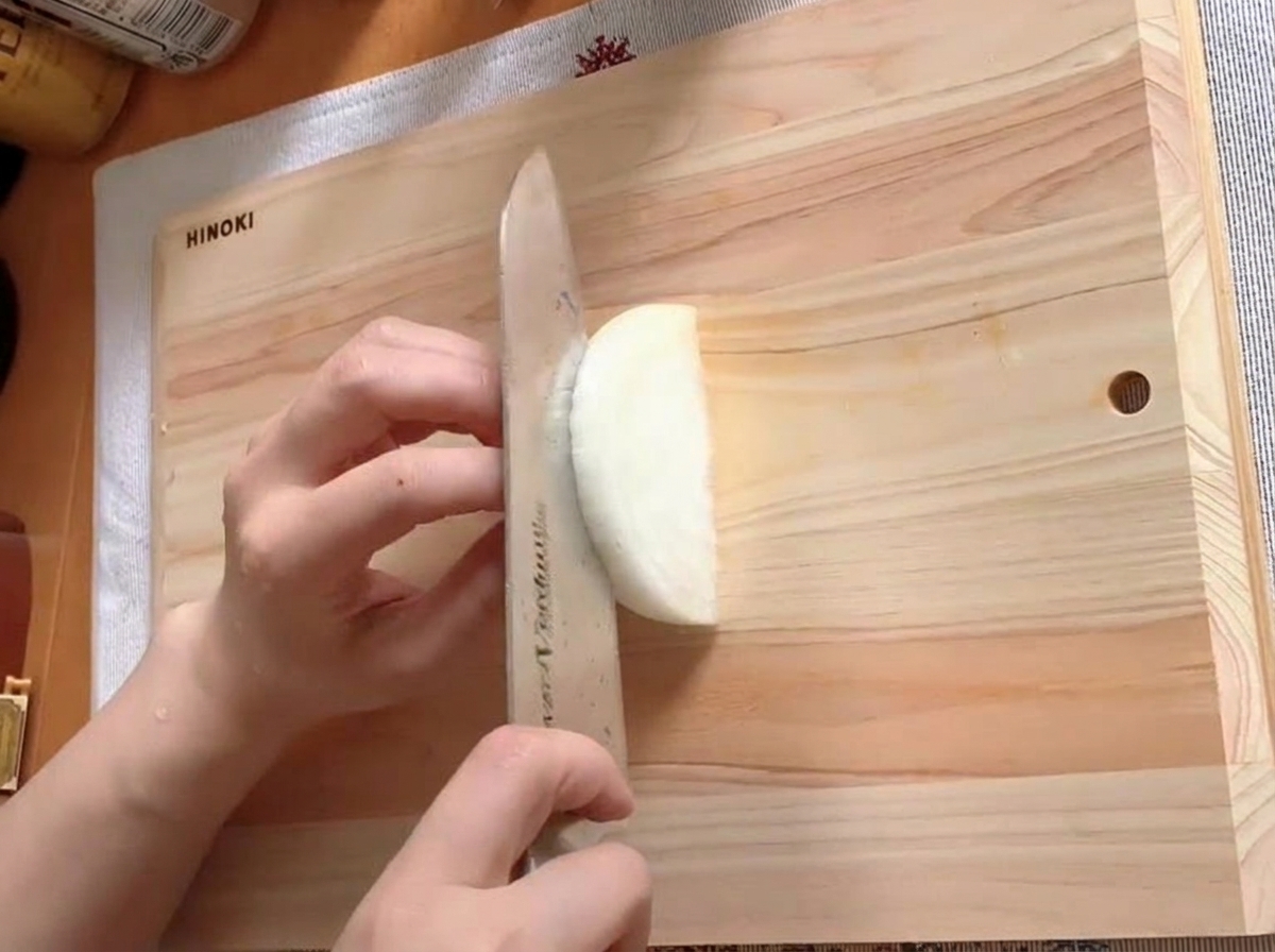 Mezza cipolla affettata sottilmente su un tagliere di legno.