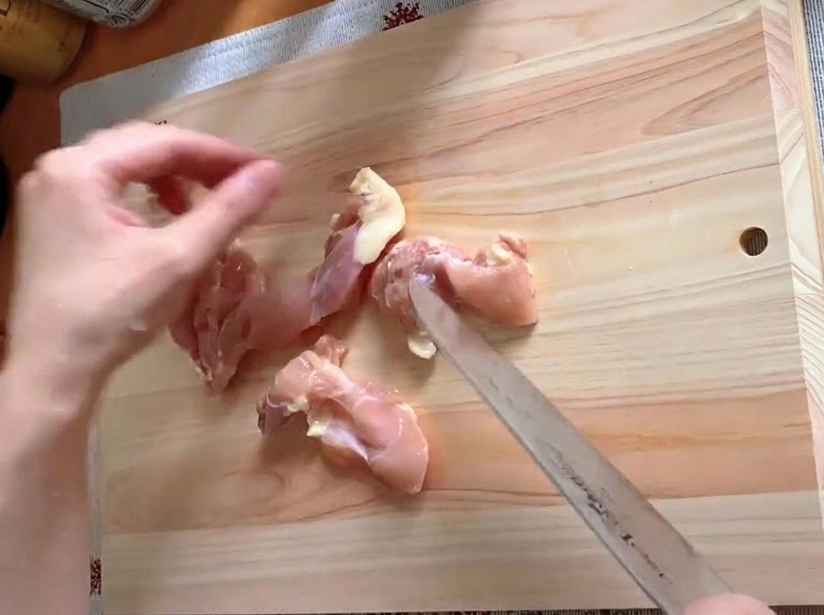 Coscia di pollo rifilata e tagliata a pezzi su un tagliere.