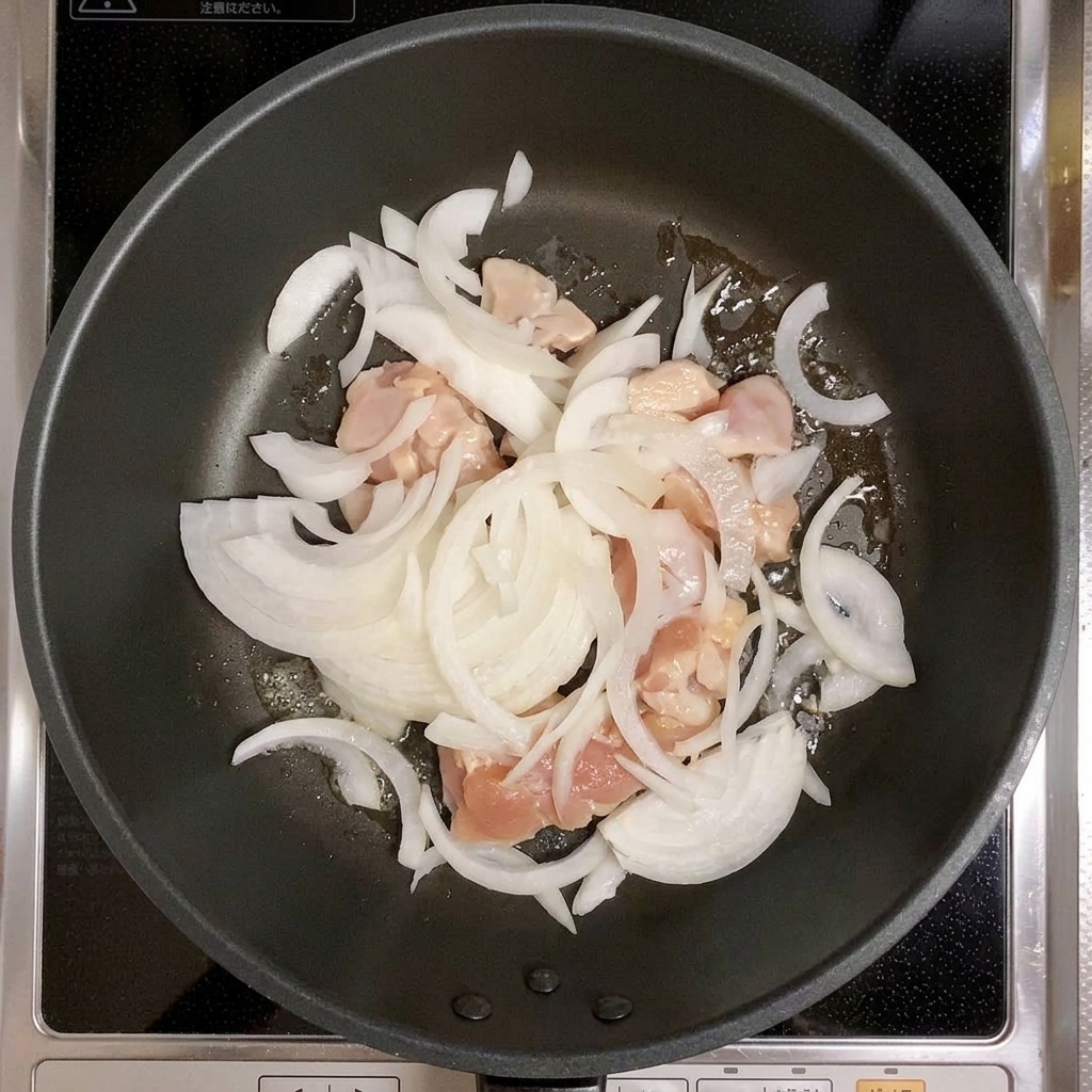 Pollo e cipolle affettate mescolati in una padella.