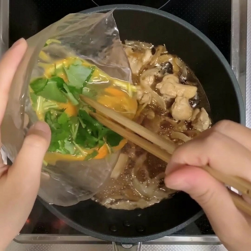 Due terzi del composto di uova e mitsuba versati nella padella con pollo e cipolle.