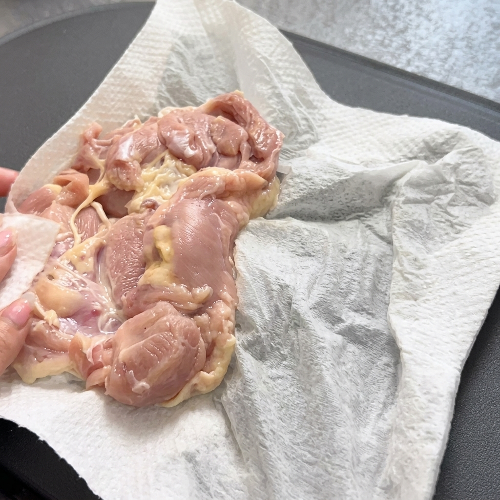Luso di pinze per posizionare delicatamente una coscia di pollo cruda in una padella calda.