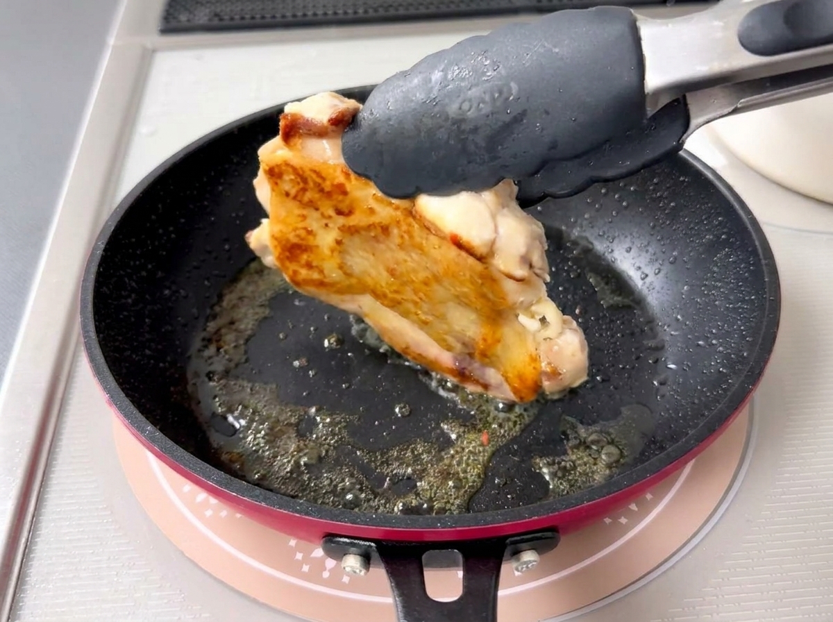 Primo piano di pinze che girano un pezzo di pollo per rivelare una pelle perfettamente dorata e croccante.