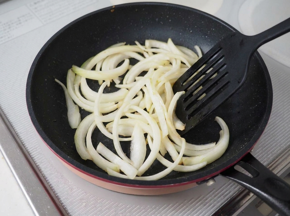 Cipolle affettate saltate in una padella antiaderente scura con una spatola nera.